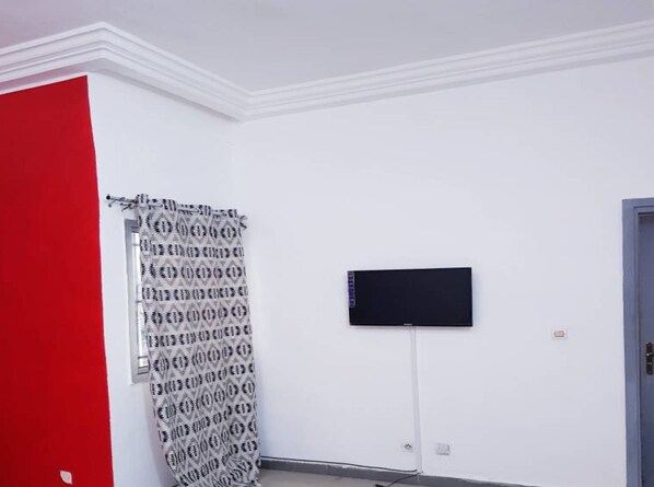 A room with a red wall, a patterned curtain, a flat-screen TV mounted on the wall, and a door.