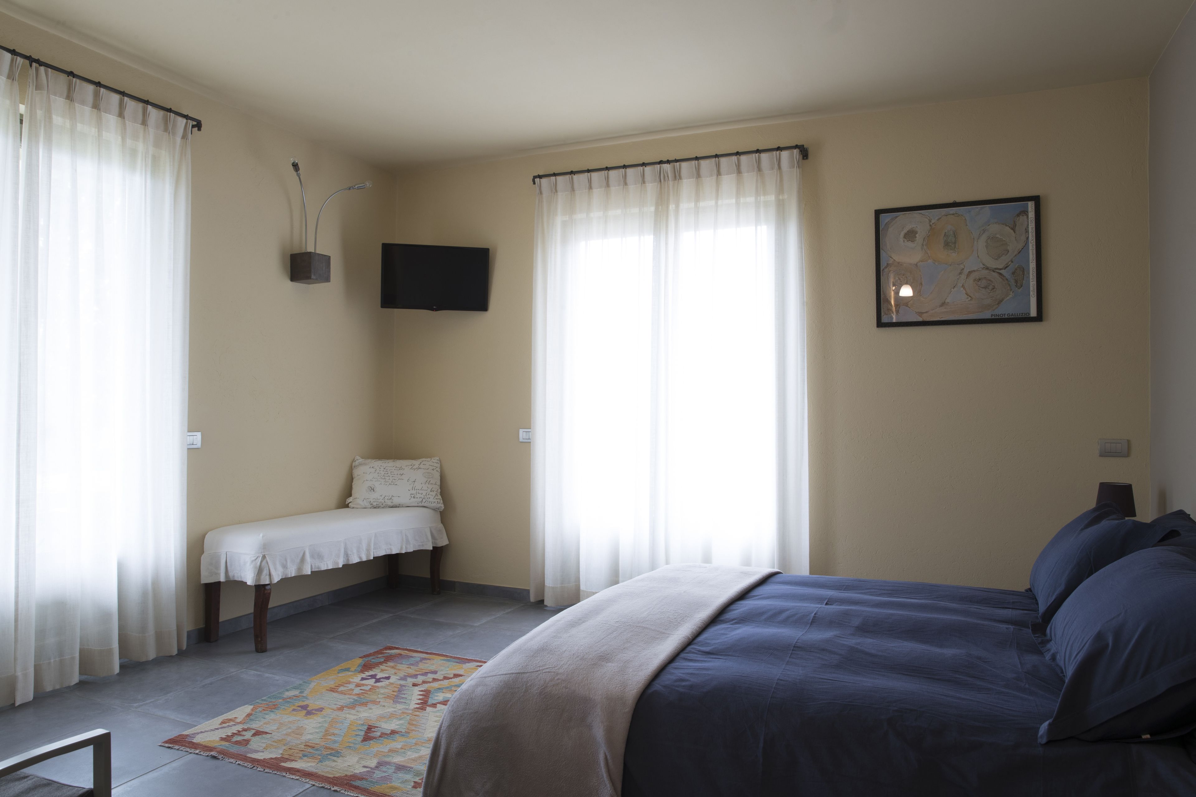 A bedroom with a bed, a bench, a TV, and a window with curtains.