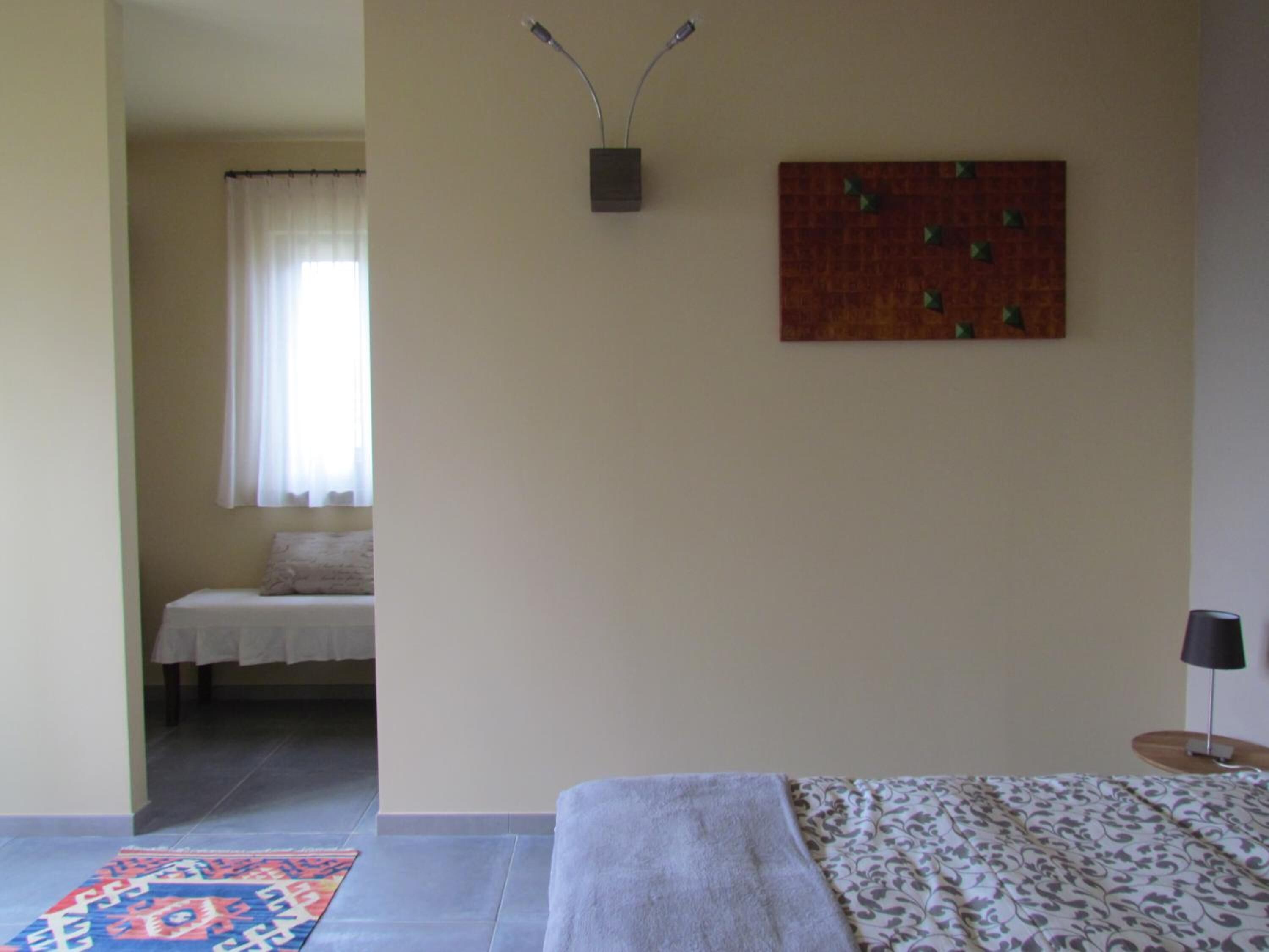 Een slaapkamer met een bed, nachtkastje, lamp, wandlamp en schilderij.