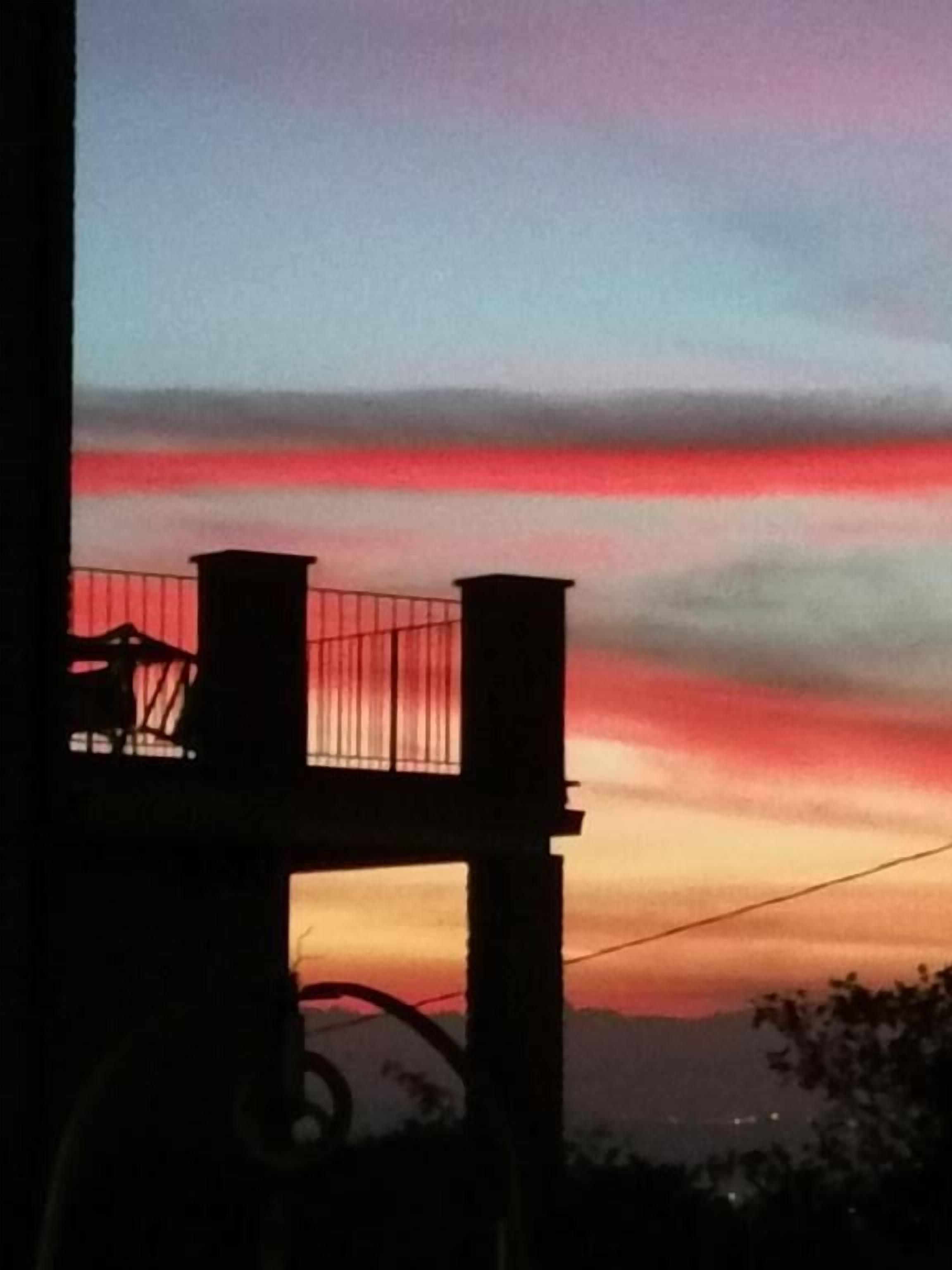 Un balcón con barandilla que da a un atardecer con cielo rojo y naranja.