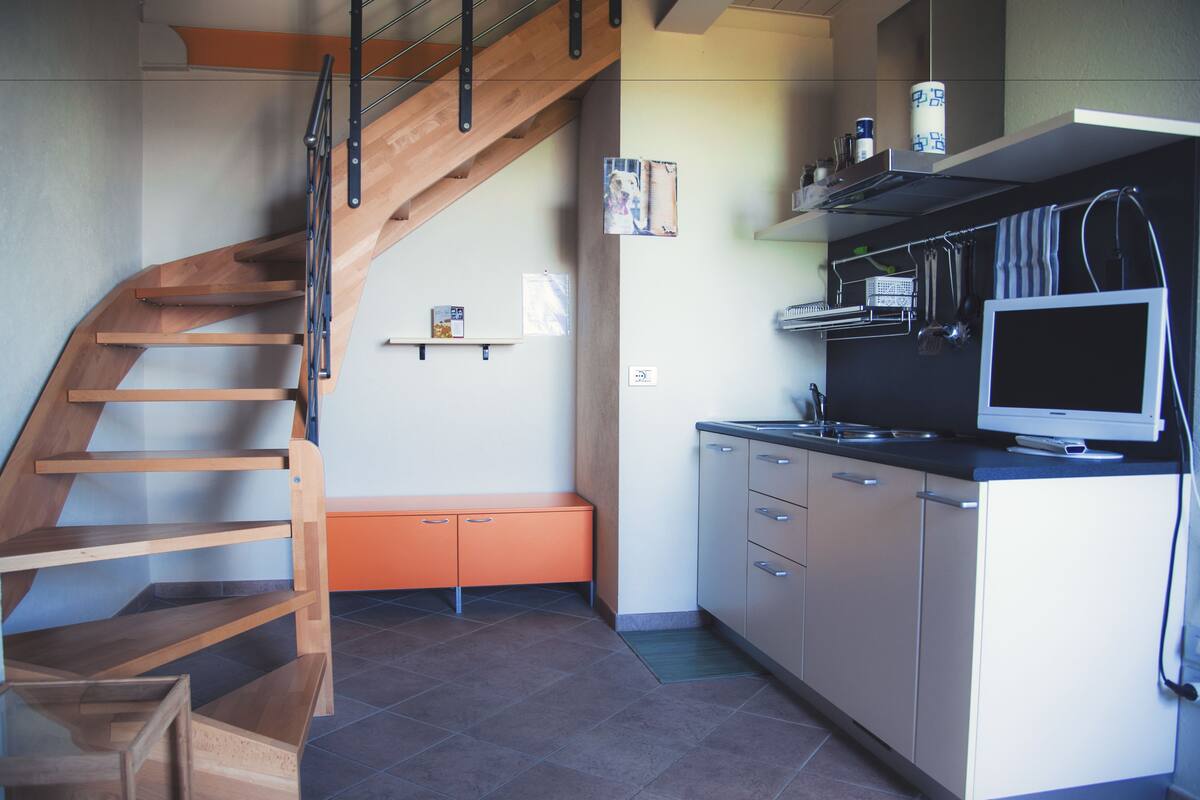 A modern kitchen with a wooden staircase, built-in cabinets, and a large window.