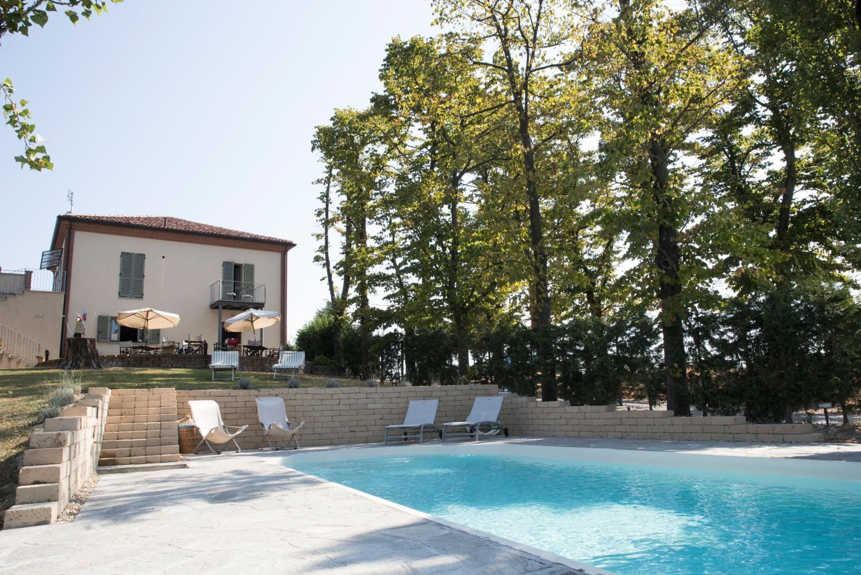A swimming pool with lounge chairs and umbrellas, a building with a tiled roof, and trees in the background.