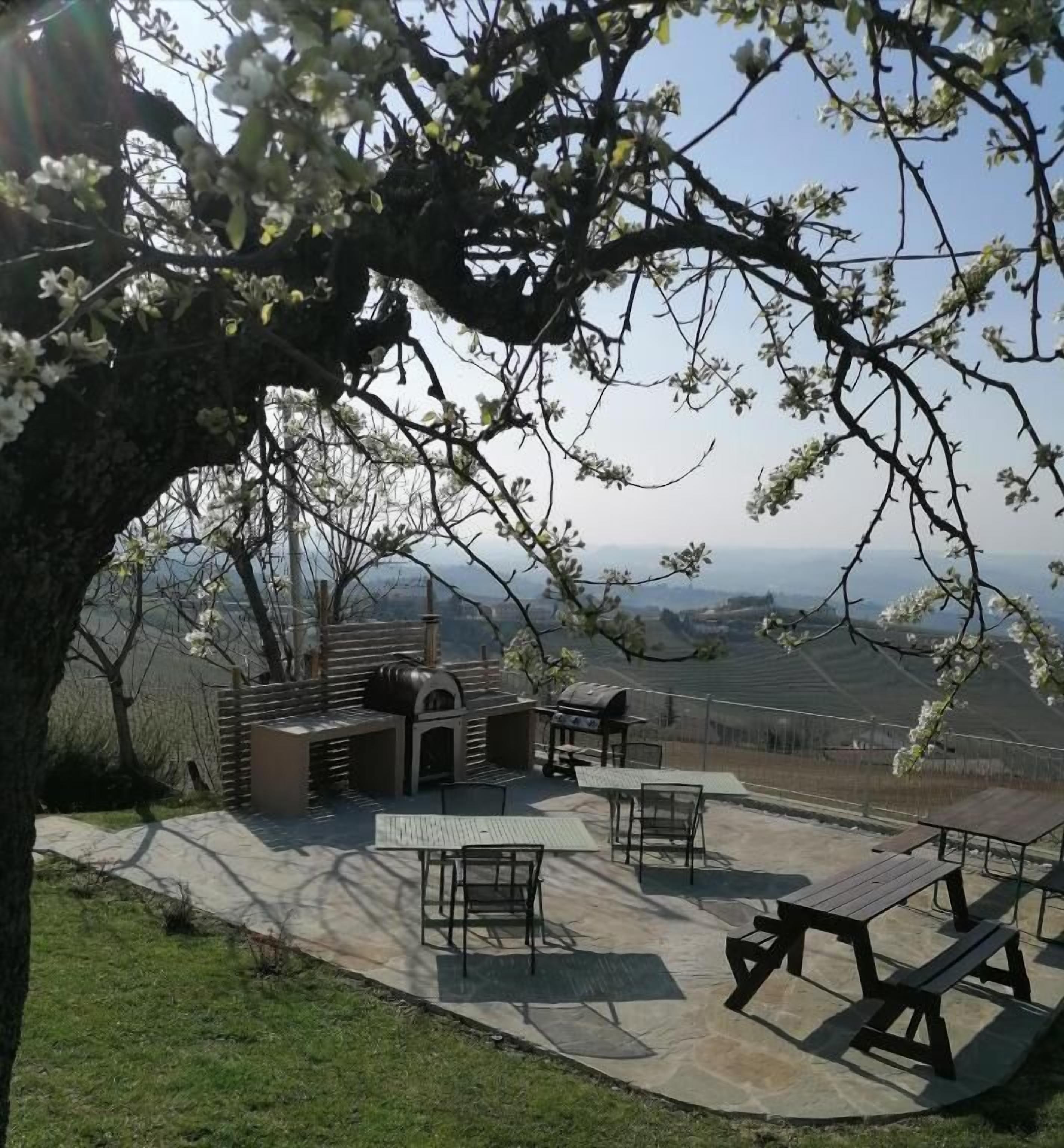 An outdoor patio area with a stone floor, picnic tables, and a barbecue grill.