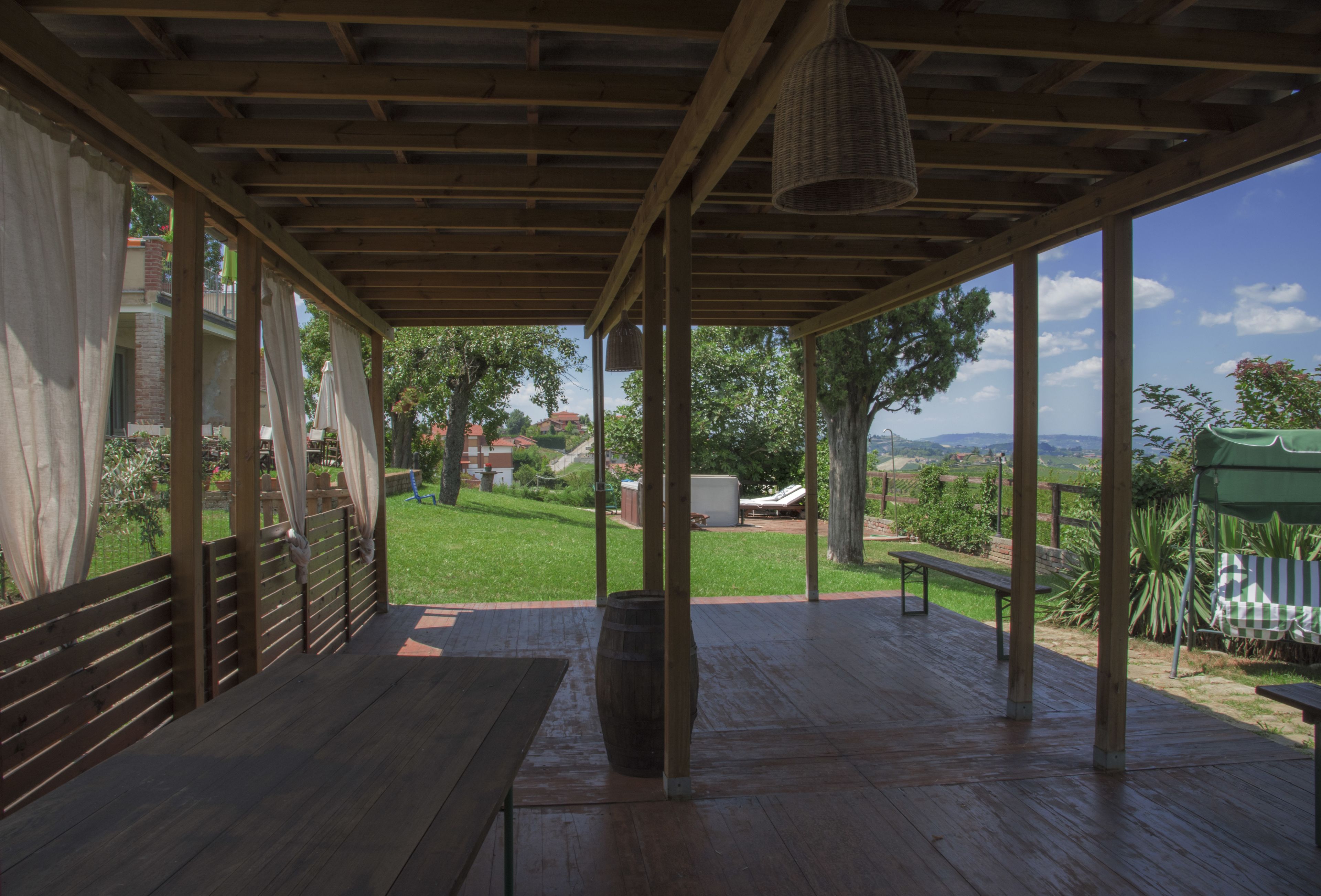 A covered outdoor area with wooden flooring, a large barrel, and a view of a grassy yard and distant hills.