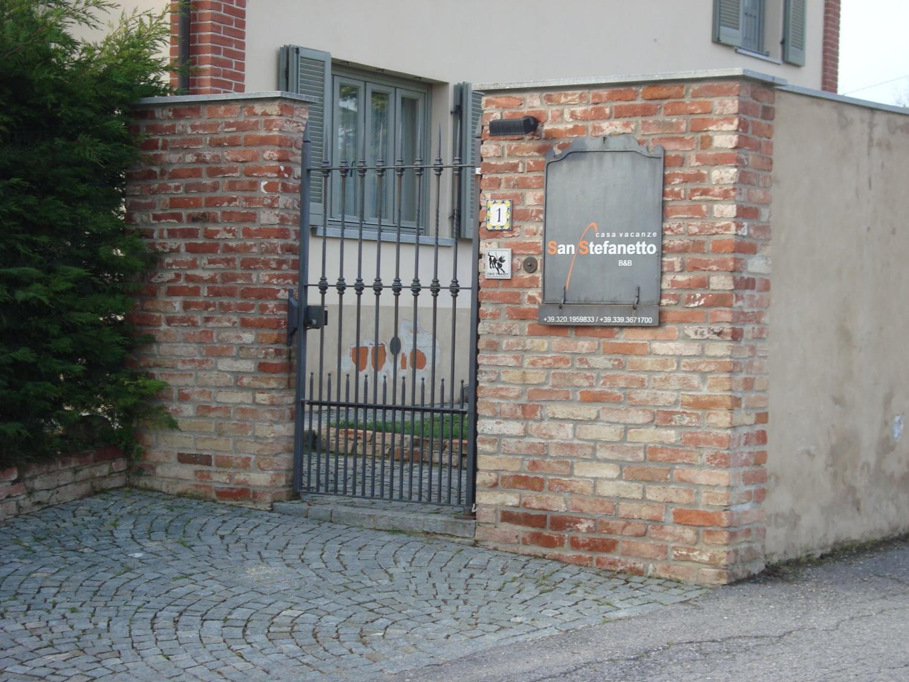 A brick building with a metal gate, a sign indicating 'casa vacanze San Stefanutto', and a small outdoor area with a paved surface.
