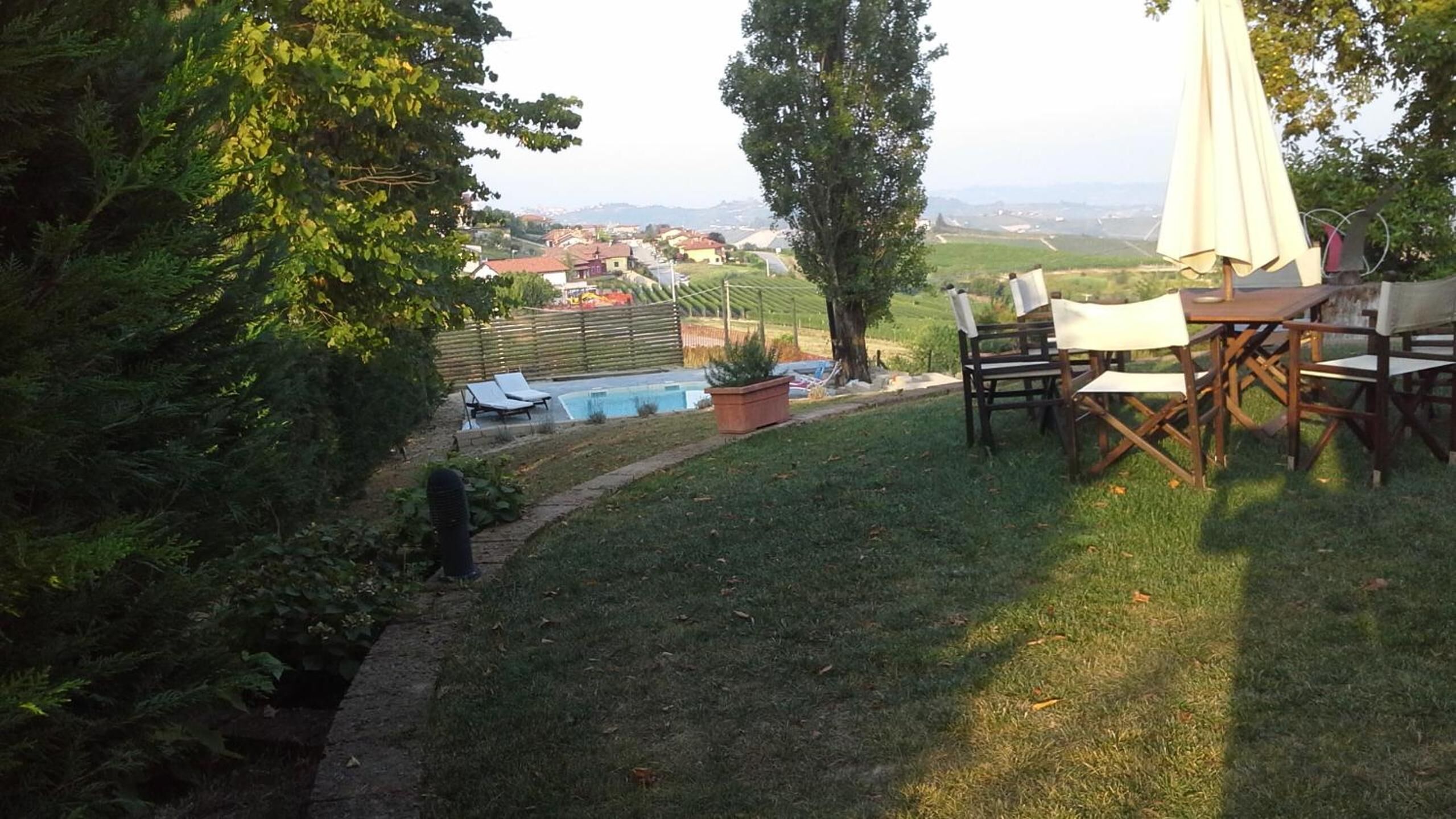 Un patio trasero con una piscina, un área de comedor con sillas y una mesa, y una vista de un pueblo a lo lejos.