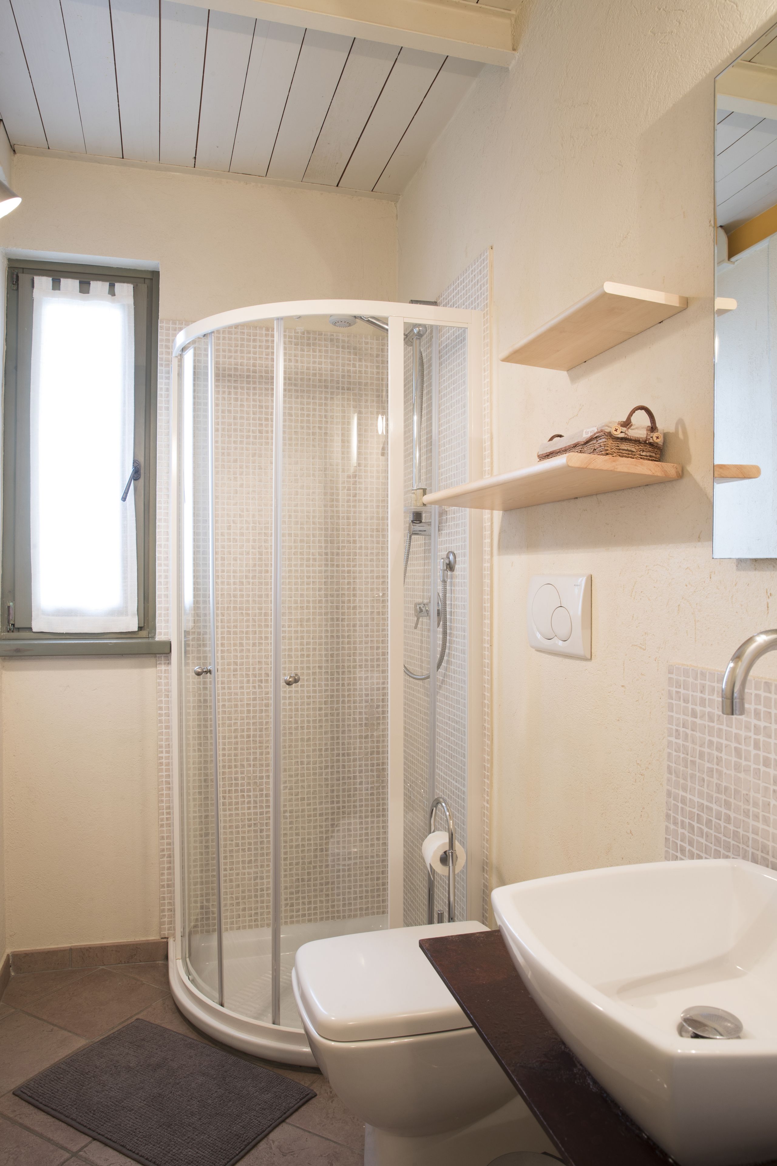 A bathroom with a glass-enclosed shower, a toilet, a sink, and a window.