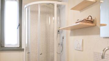 A bathroom with a glass-enclosed shower, a toilet, a sink, and a window.