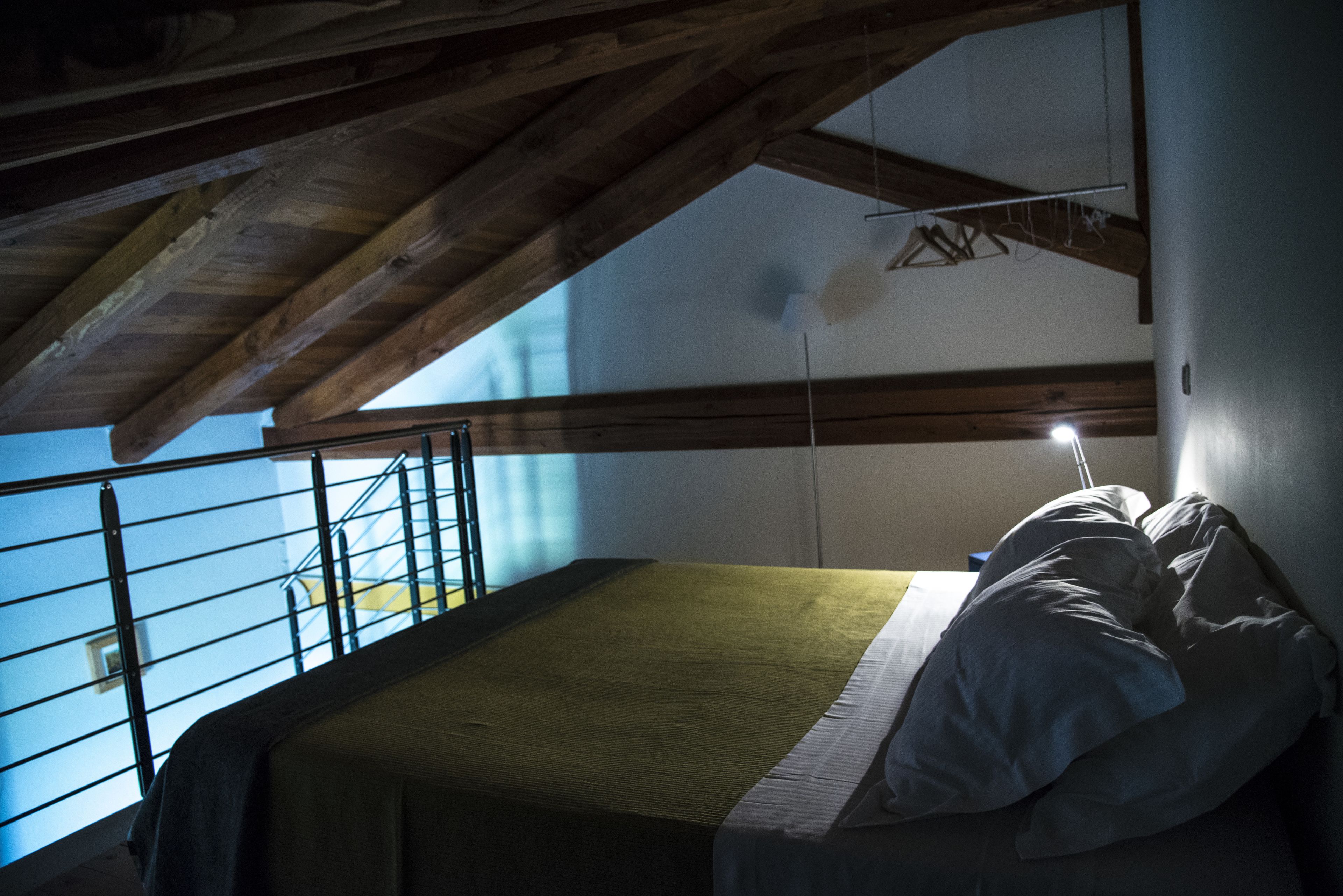 Ein Schlafzimmer mit Bett, Holzbalken, einem Balkon und Blick zum Himmel.