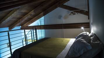 Ein Schlafzimmer mit Bett, Holzbalken, einem Balkon und Blick zum Himmel.
