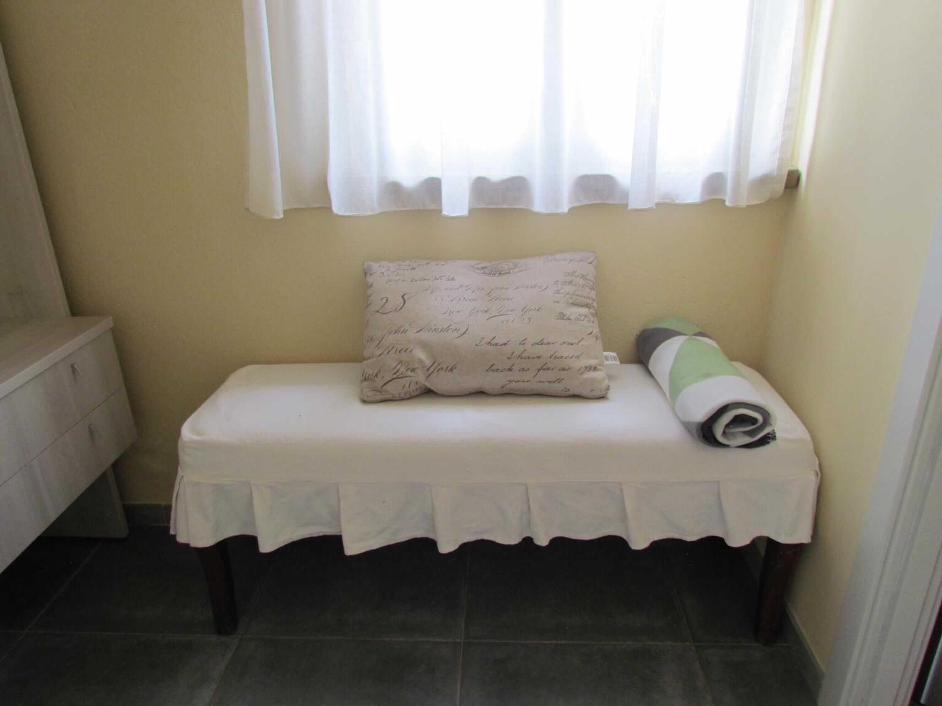 Un baño pequeño y ordenado con un banco, una almohada con notas escritas a mano y una toalla enrollada.