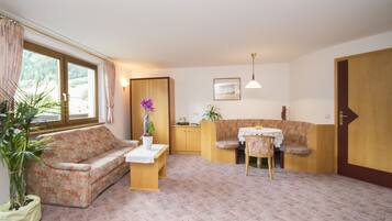 Una habitación acogedora con un sofá floral, una pequeña mesa de comedor con sillas, una planta en maceta y una puerta de madera.
