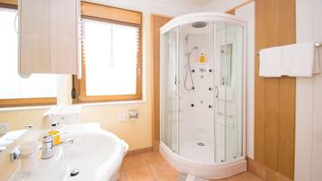 Une salle de bain moderne dotée d’une douche à parois de verre, d’une baignoire et d’une fenêtre laissant entrer la lumière naturelle.
