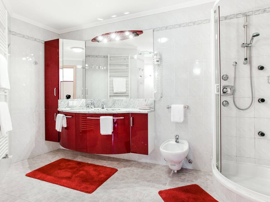 Casa de banho moderna com cabine de duche em vidro, sanita higiénica e toucador com armário vermelho e bancada branca.