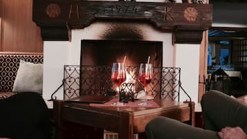 A cozy room with a fireplace, two glasses of red wine on a table, and a patterned sofa.