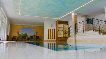 A modern indoor swimming pool with a clear ceiling, a wooden staircase, and a mural on the wall.