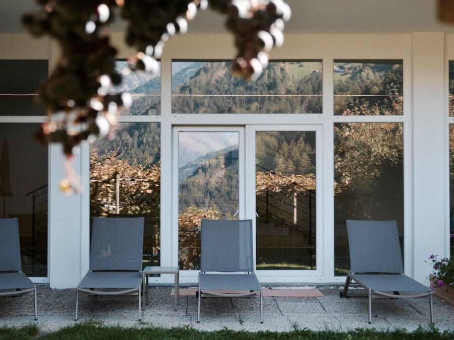 Un espace extérieur abrité, doté de trois chaises et de grandes fenêtres offrant une vue sur un paysage montagneux.