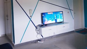 En moderne stue med et fladskærms-tv på et hvidt tv-møbel, et vægmonteret lydsystem og en dør til højre.
