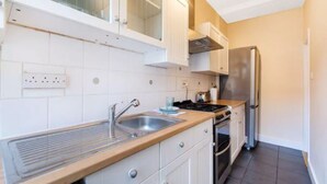 A modern kitchen with white cabinets, a stainless steel refrigerator, and a built-in oven. - Simon Apartment - London Launchpad (London)