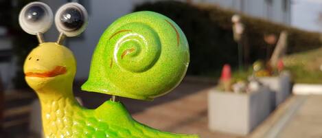 Una escultura decorativa de caracol, con concha verde y cuerpo amarillo, ubicada al aire libre frente a un edificio.
