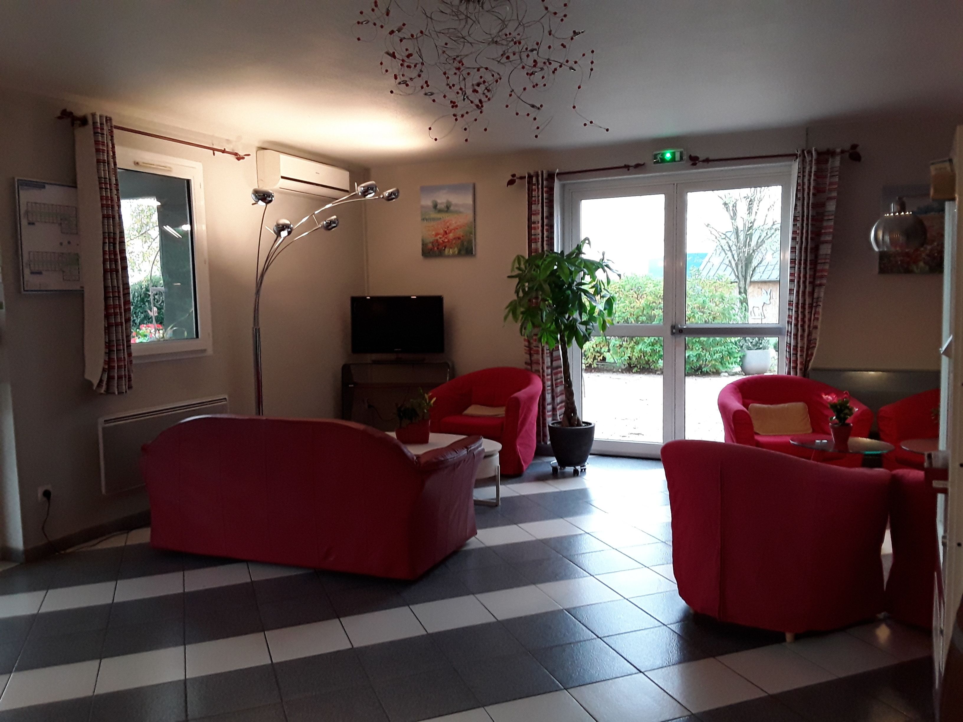 A room with red sofas, a potted plant, a flat-screen TV, and a large window with curtains.