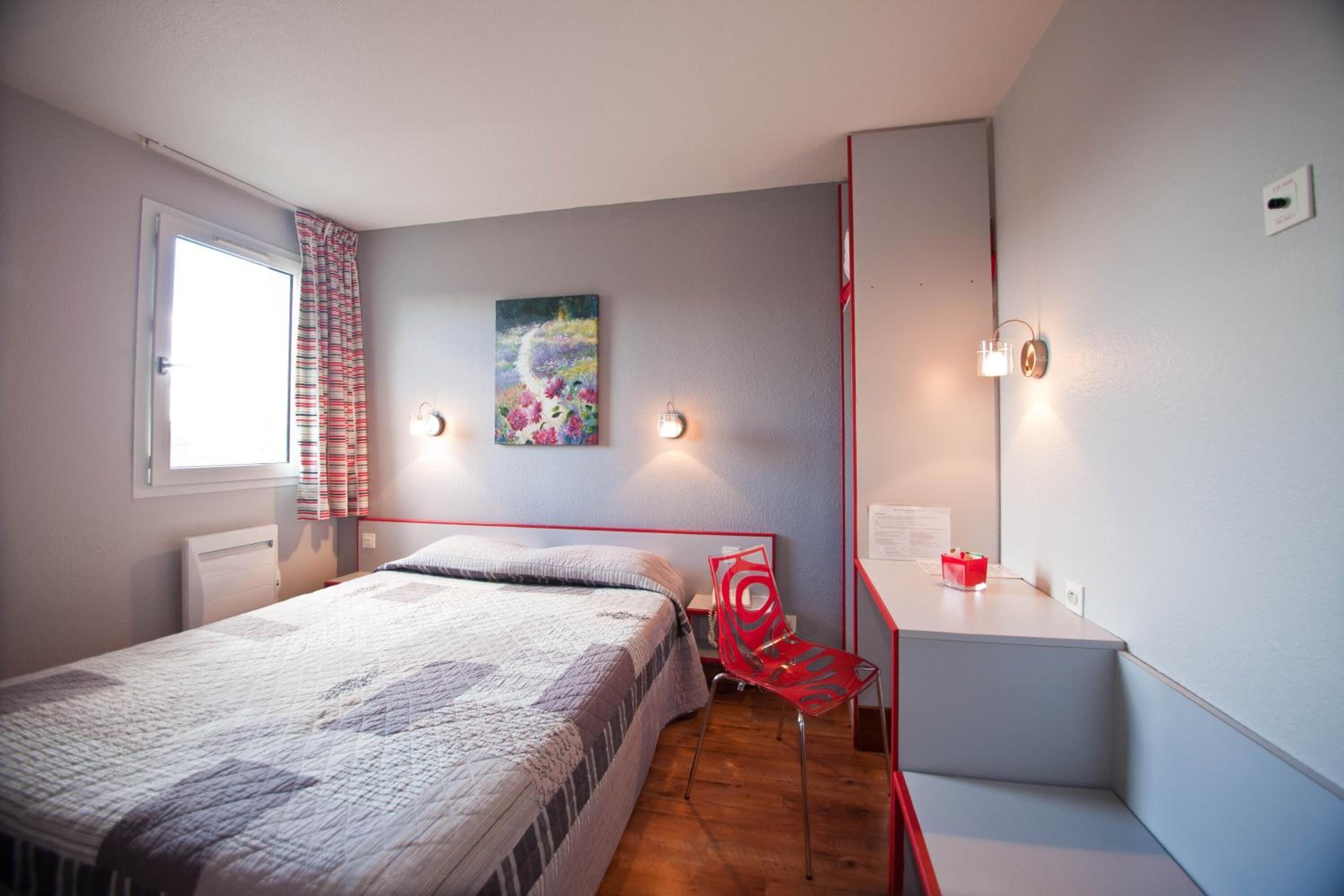 A bedroom with a bed, a chair, a desk, and a painting on the wall.