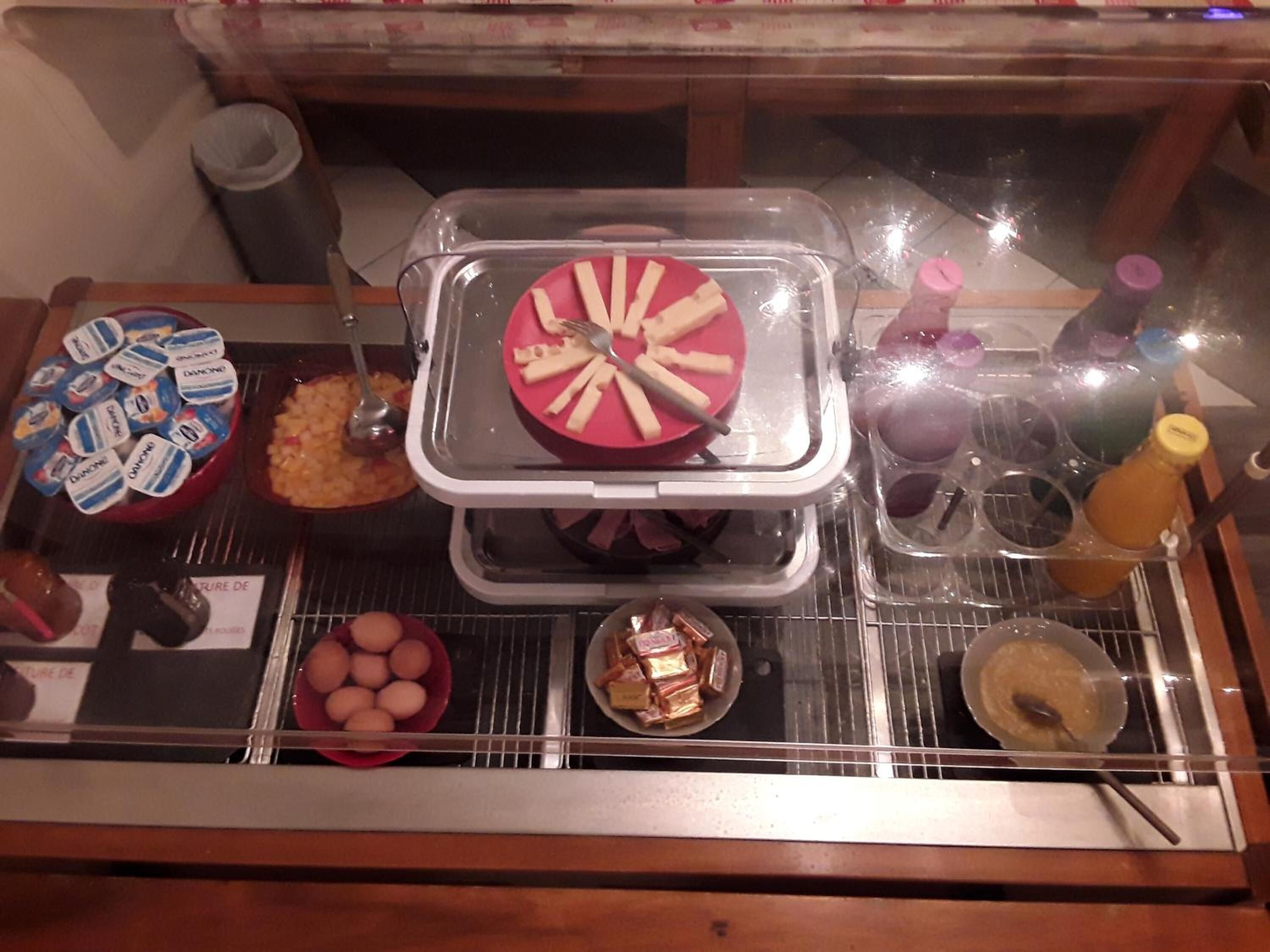 Un bufé con diferentes opciones de comida, incluyendo una bandeja de carnes cortadas, un tazón de huevos y un recipiente con pasteles.