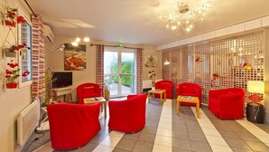 A hotel lobby with red sofas, a TV, and a large window with a view of greenery. - La Grange de Marie (Nitry)