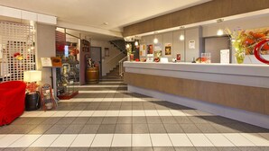 A hotel reception area with a modern design, a reception desk, a staircase, and a seating area with a red chair. - La Grange de Marie (Nitry)