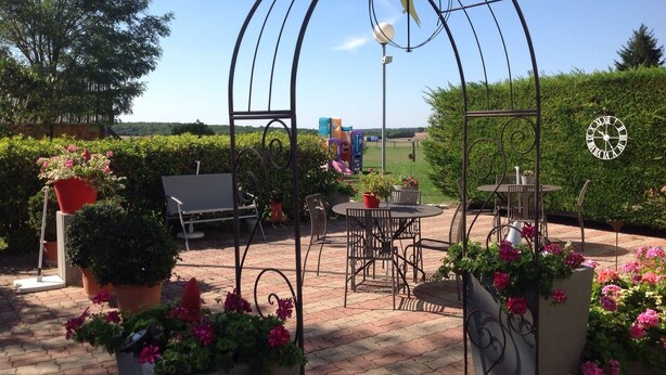 A patio area with a metal archway, outdoor seating, potted plants, and a clock on the wall. - La Grange de Marie (Nitry)