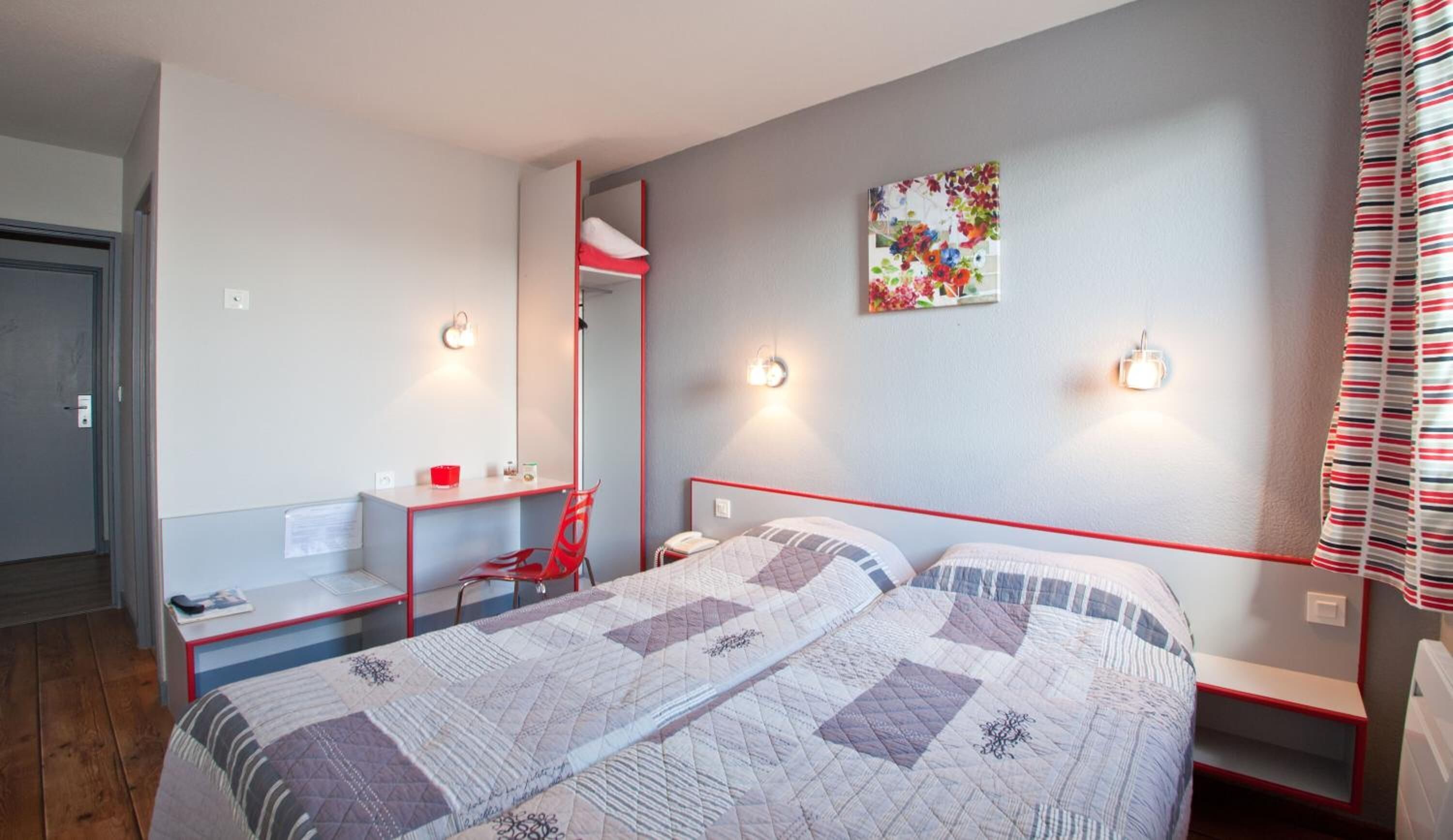 Un lit double avec une couette, un bureau avec une chaise, un téléphone et un luminaire fixé au mur.