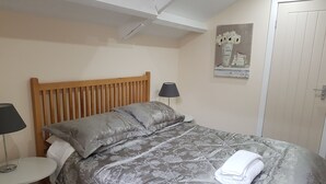 A neatly made bed with a grey floral duvet, a wooden headboard, a small bedside table with a lamp, and a framed picture on the wall. - Church View (Huddersfield)