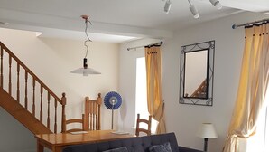 A living room with a dark blue sofa, wooden dining table, and chairs. There is a staircase with wooden railings, a chandelier, and a mirror on the wall. - Church View (Huddersfield)