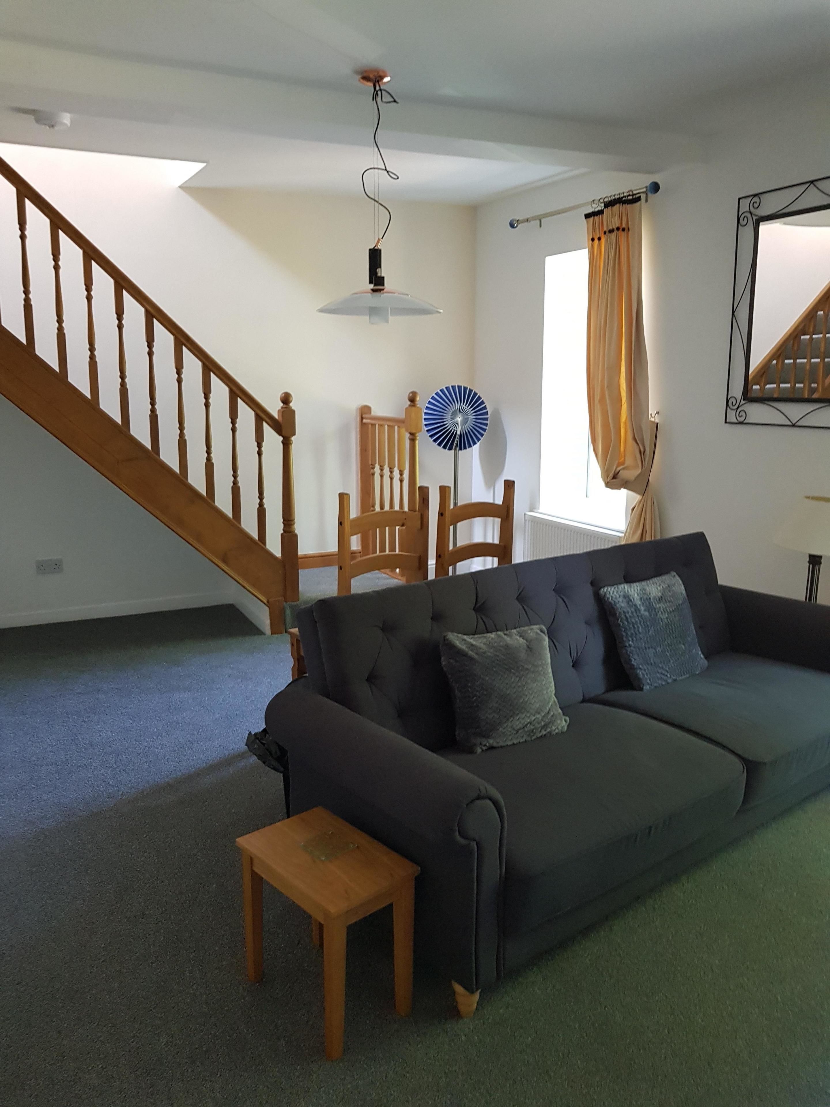 A living room with a dark green sofa, a wooden coffee table, a blue fan, and a staircase.