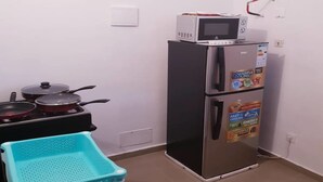 A compact kitchen with a microwave, a refrigerator, and a stove with pots.