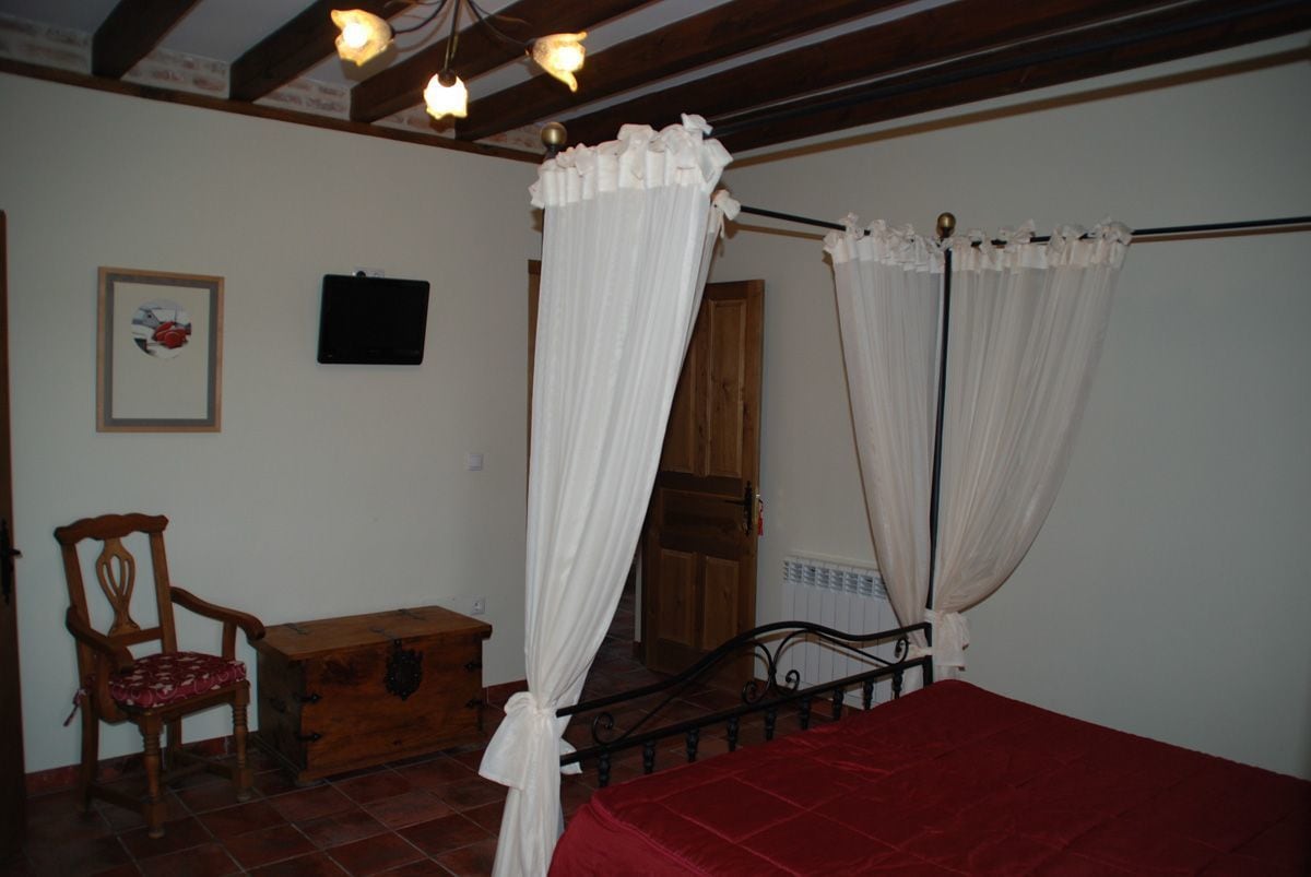 Un dormitorio con una cama con dosel, una silla de madera, un aparador y un cuadro en la pared.