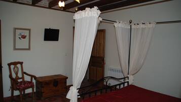 Un dormitorio con una cama con dosel, una silla de madera, un aparador y un cuadro en la pared.