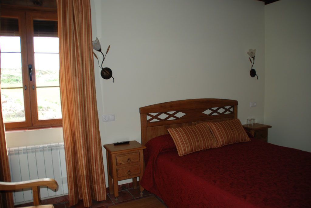 Un dormitorio con cama de madera, una mesita de noche, una silla y una ventana con cortinas.