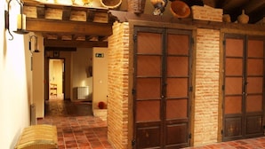 Interior rústico com piso de azulejos, teto de madeira e parede de tijolos. Há cestos e um enfeite de galo na parede.