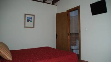 Een slaapkamer met een rode sprei, een houten deur naar een badkamer en een ingelijst beeld aan de muur.