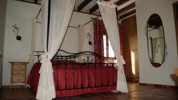 A four-poster bed with red bedding, a wooden nightstand, a mirror, and a red curtain.