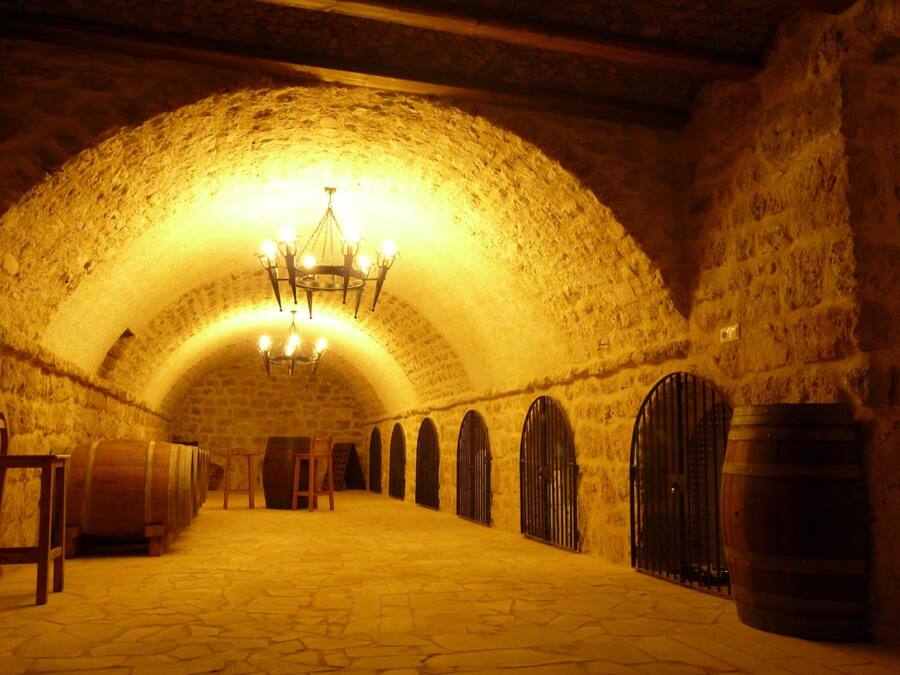 Una bodega de piedra con barriles de madera y un candelabro.