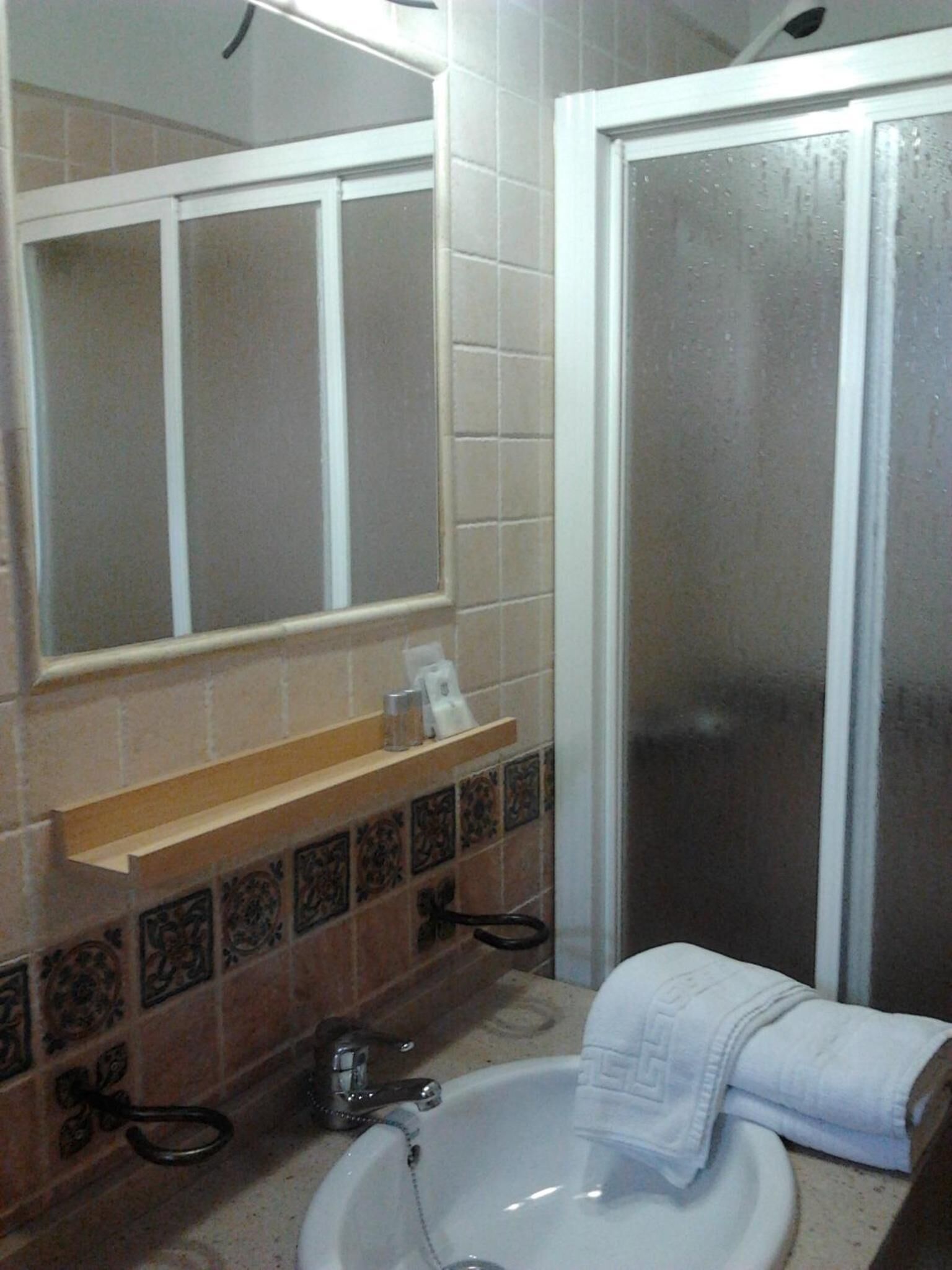 Un baño con lavamanos blanco, espejo, toalla y puerta de ducha.