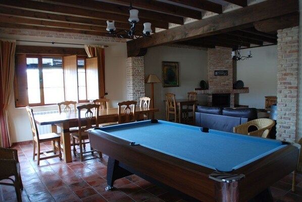 A pool table in a room with a brick fireplace, wooden furniture, and a dining area.