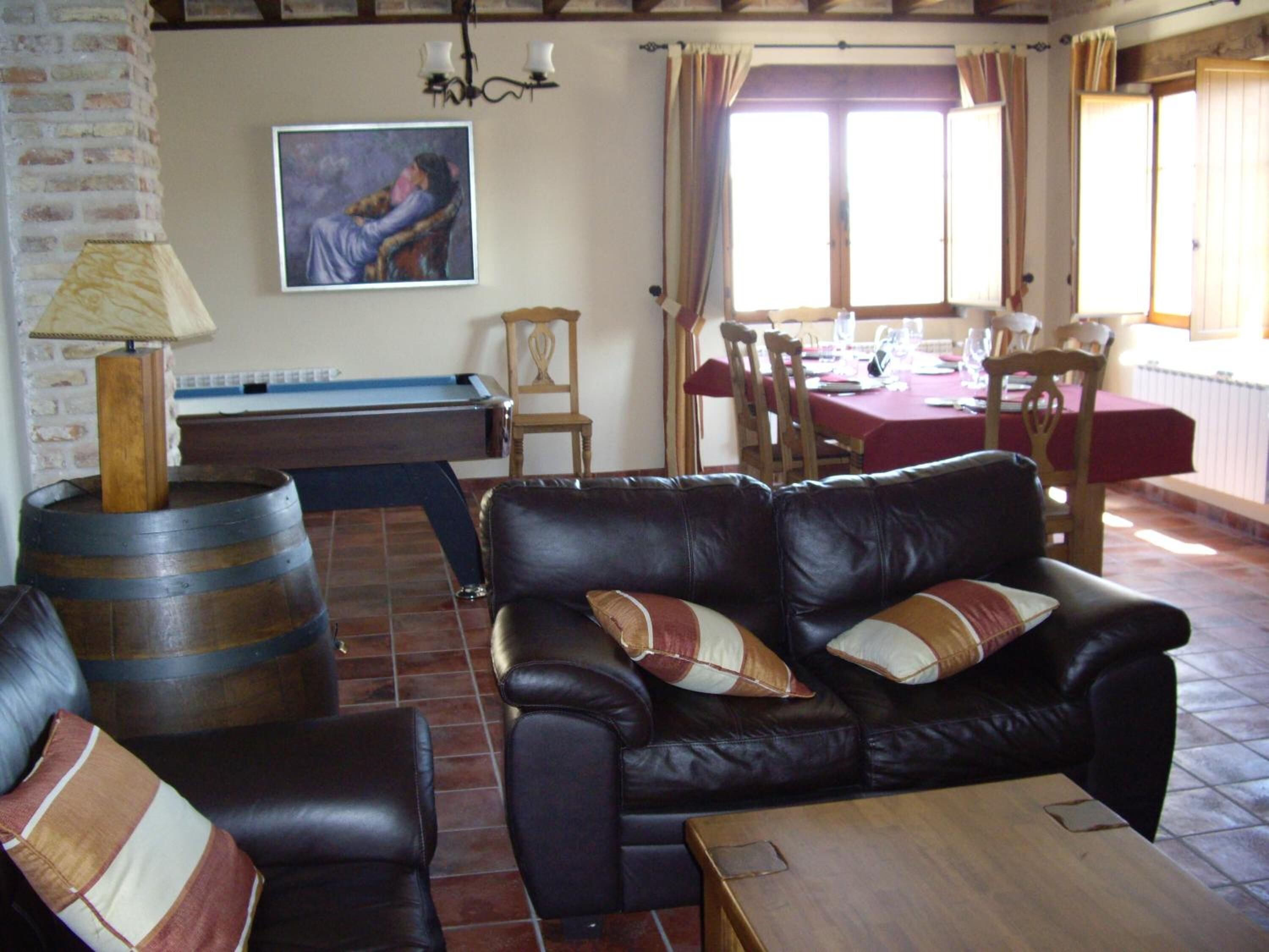 Una sala de estar con mesa de billar, sofá de cuero y comedor con mesa y sillas.