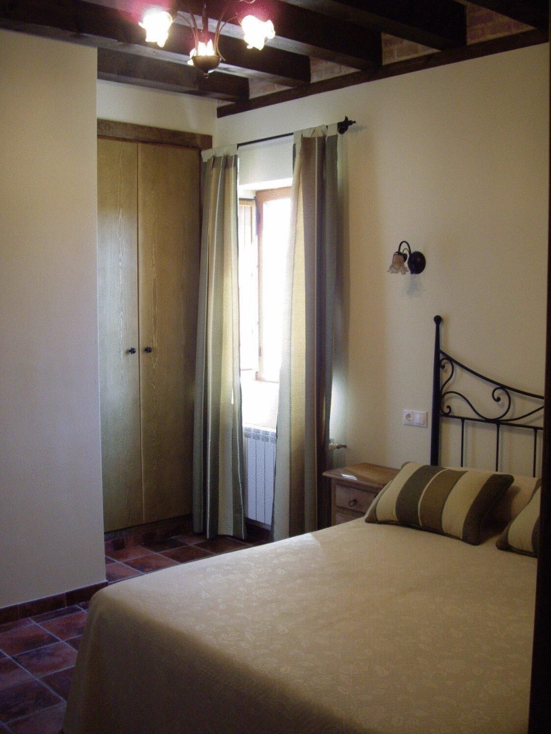 Une chambre à coucher comprenant un lit, une table de chevet, une lampe fixée au mur et une porte donnant sur une autre pièce.