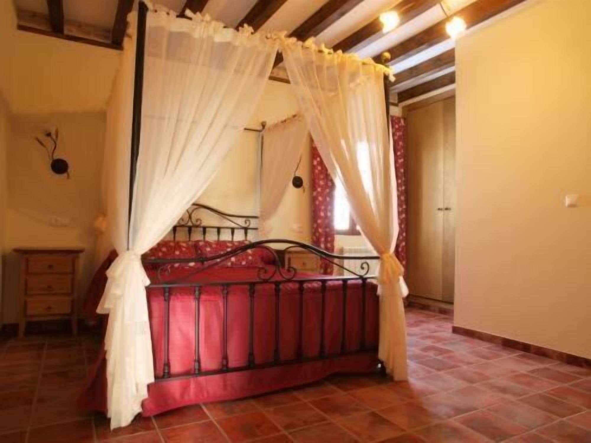 Une chambre à coucher avec un lit sous un dais, un plancher en bois et une porte au fond.