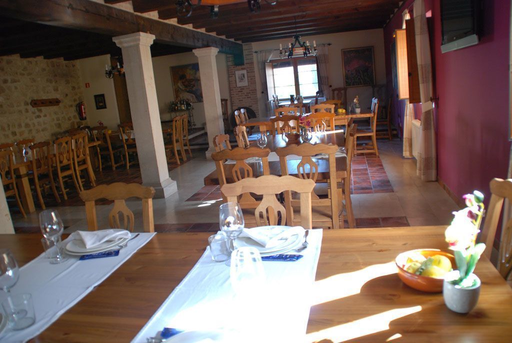 A dining area with wooden tables and chairs, a stone wall, and a window with natural light.