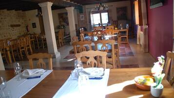 A dining area with wooden tables and chairs, a stone wall, and a window with natural light.
