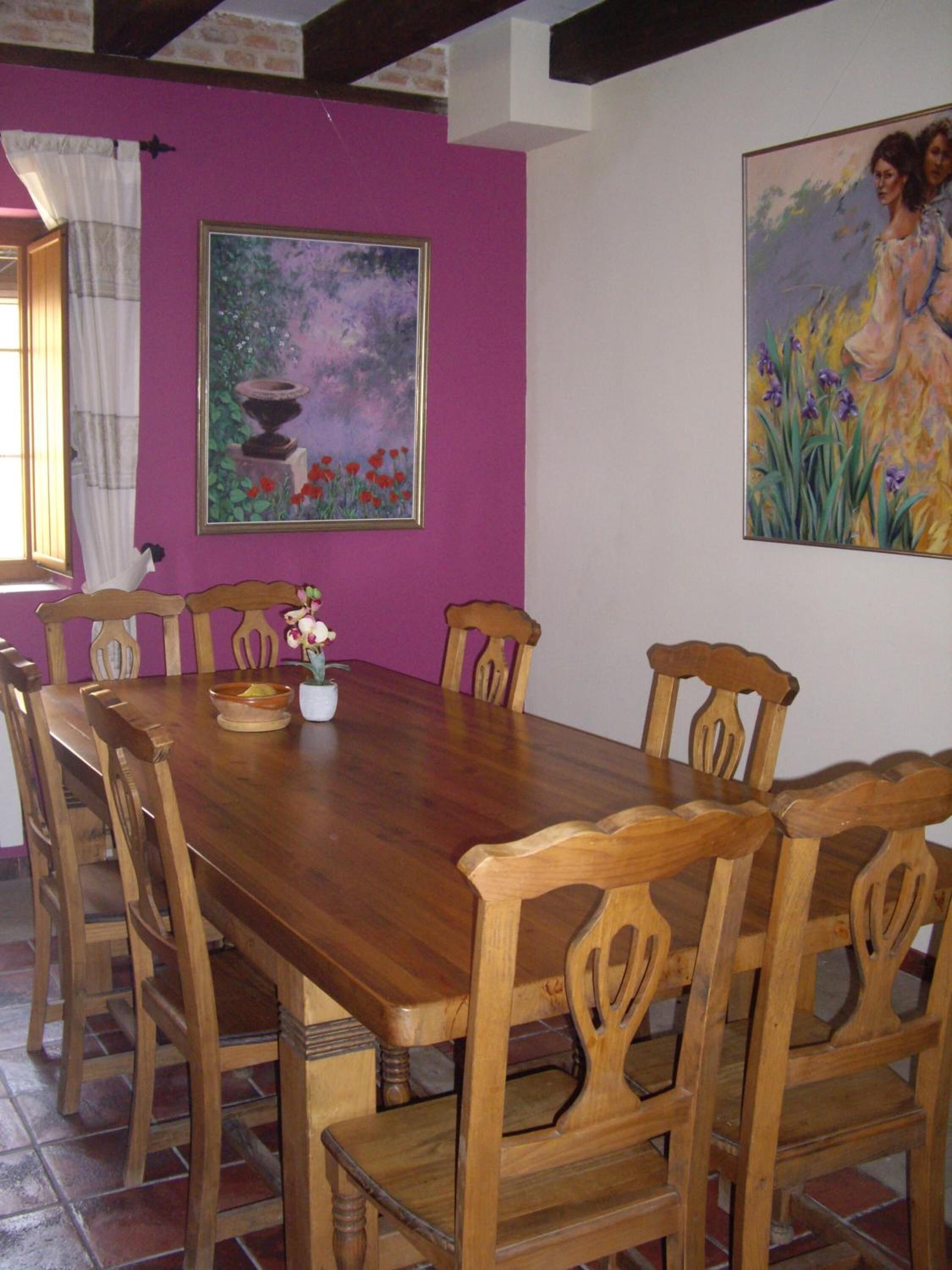 Un comedor con una mesa y sillas de madera, un cuadro en la pared y una ventana con cortinas.